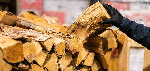 Hand selecting a kiln-dried firewood log from a stacked ECOFUEL™ SingleDeck® crate