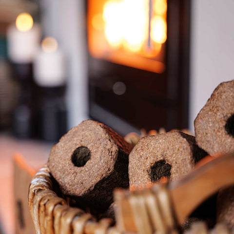 ECOFUEL Pinikay heat logs in a basket with a fireplace in the background