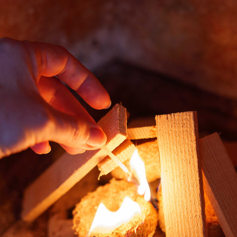 Hand lighting a wooden block with a match, surrounded by warm glow.